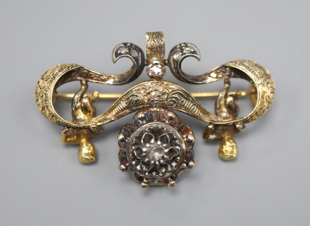 An ornate Victorian diamond set gold and silver suspension brooch, with central cluster flanked by putti holding a scroll, width 4.5cm,